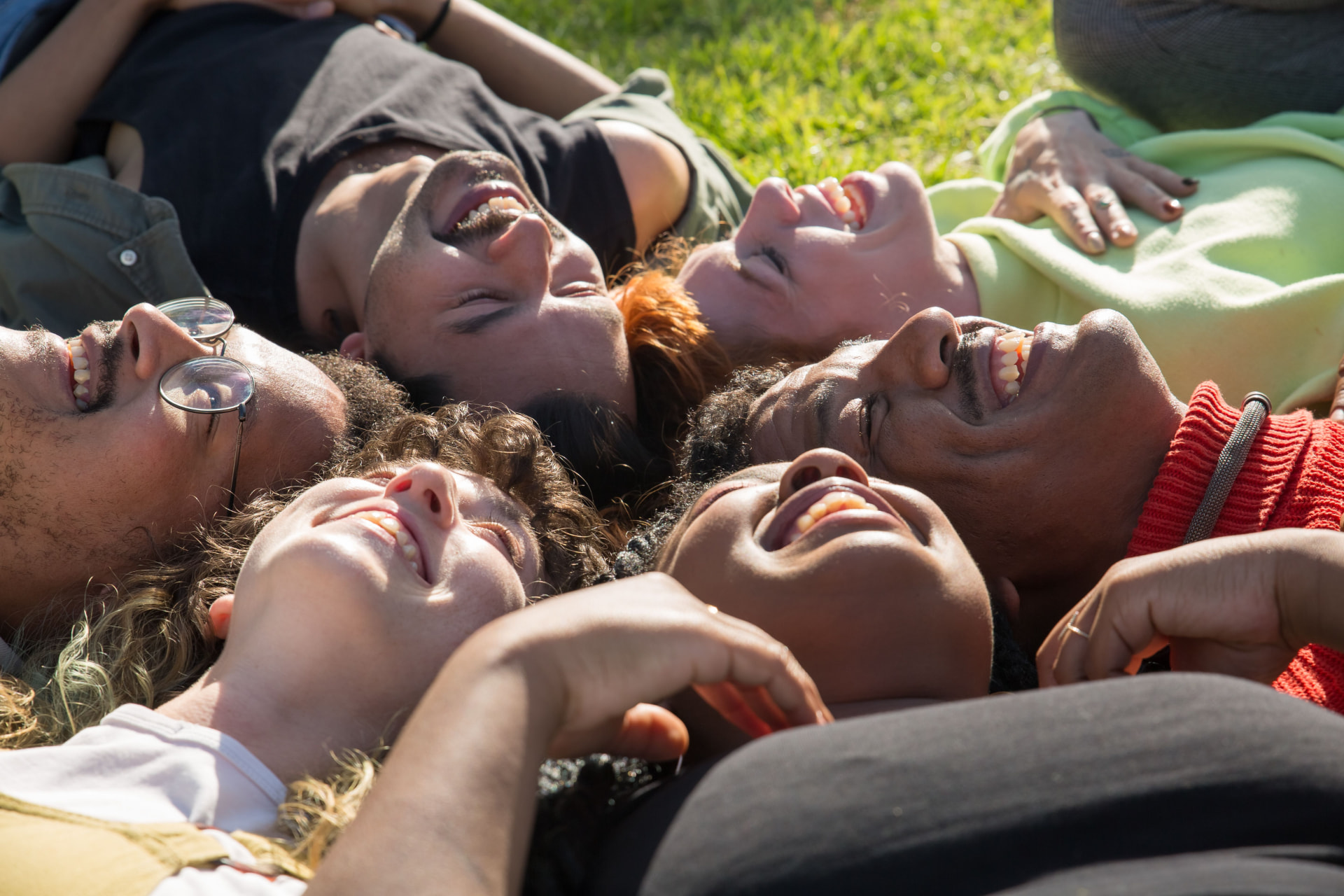 Six people lying in a circle on the grass, laughing together